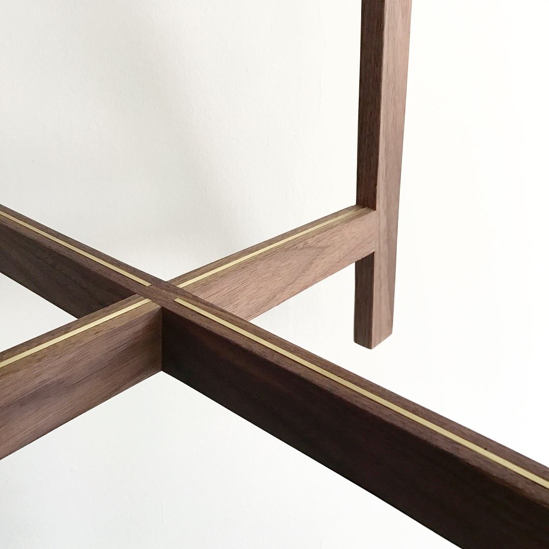 Close-up of the walnut stool's crossed stretchers, each with a thin brass inlay along its length