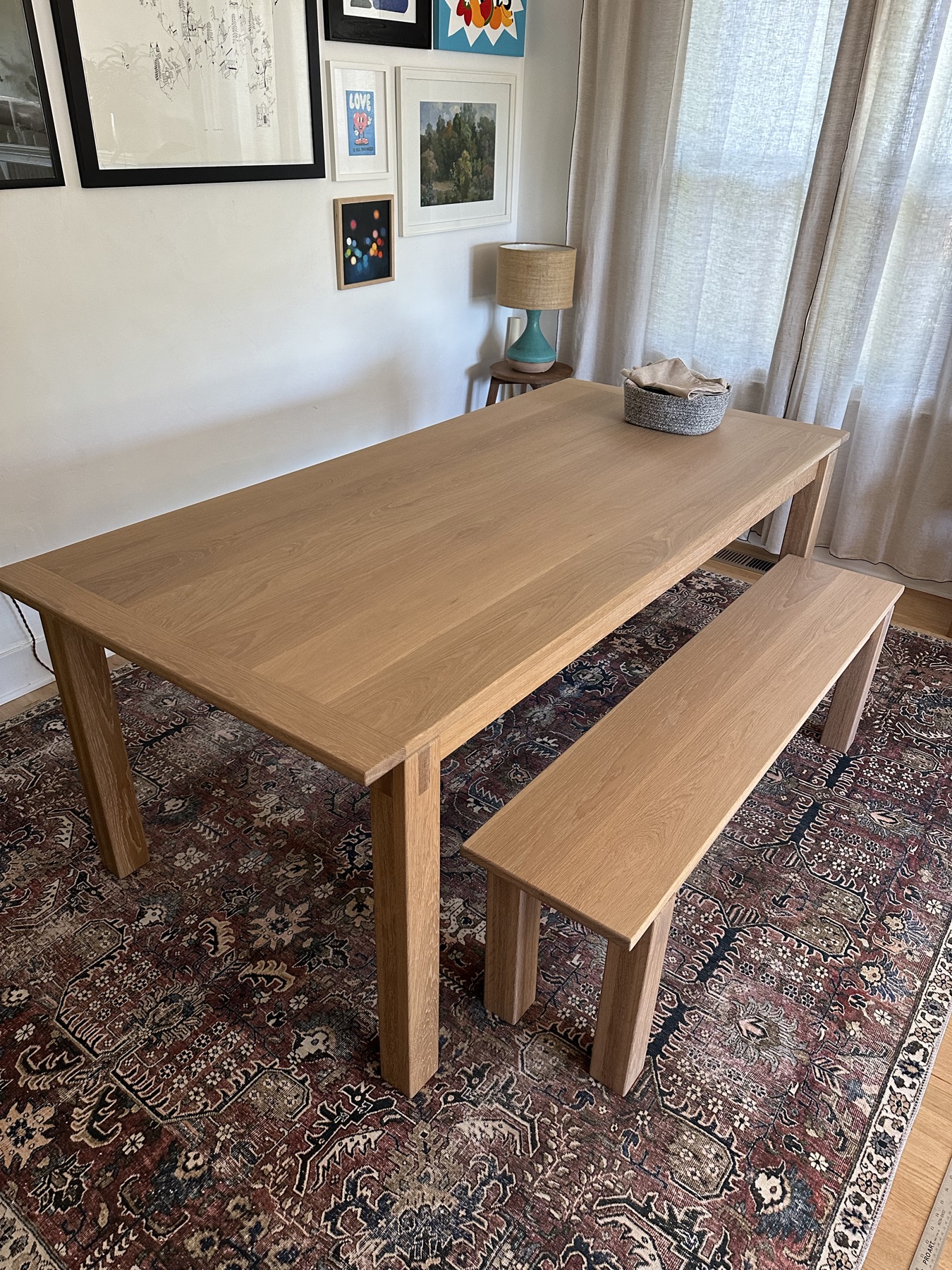 Finished light oak dining table with a matching bench, set on a patterned rug in a dining room